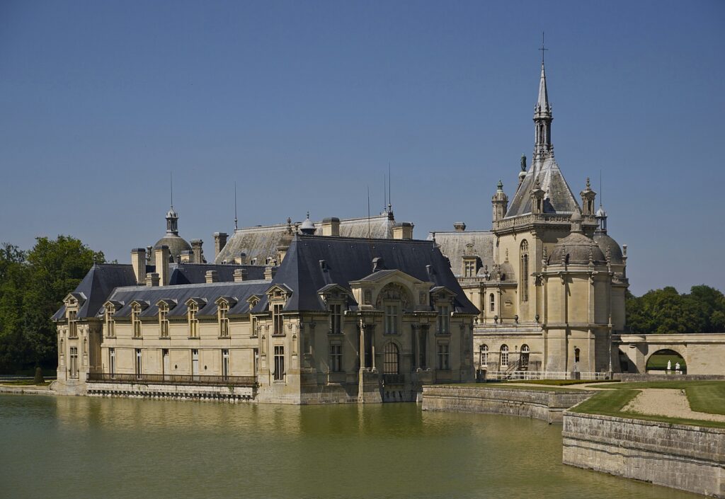 Vue générale du château de Chantilly depuis l'entrée du parc. (Visite du château de Chantilly, ses musées et son parc !). Crédit photo wikimedia commons.